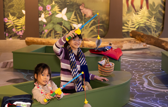 Two young girls sitting inside the boat fihing with toy fish rods.