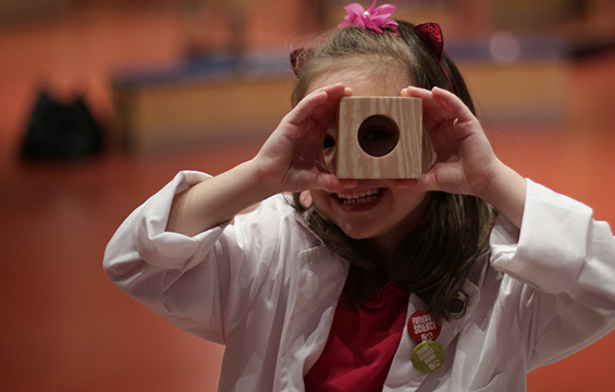 A girl looking through a wooden block with a hole in it.