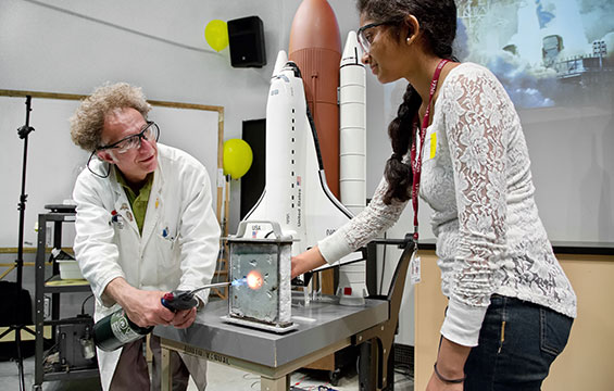 A Science Centre educator demonstrates to a student while holding a lit blow torch.