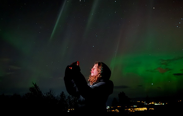 A woman uses her smart phone to take a picture of the northen lights.