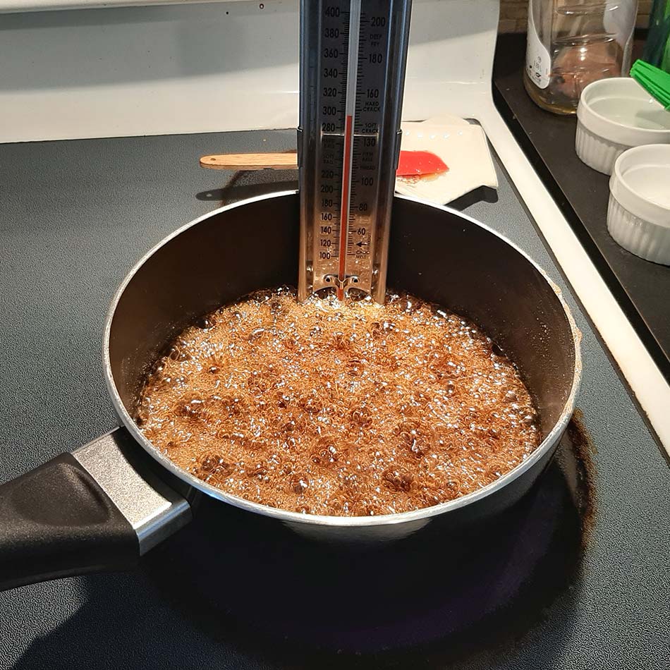 A candy thermometer sits in a pan of boiling candy.