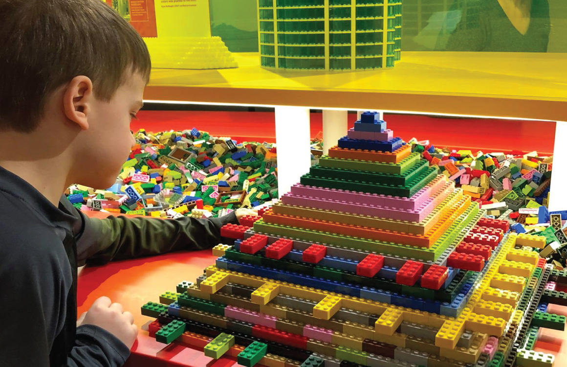 A boy works on a pyramid structure made of Lego bricks.