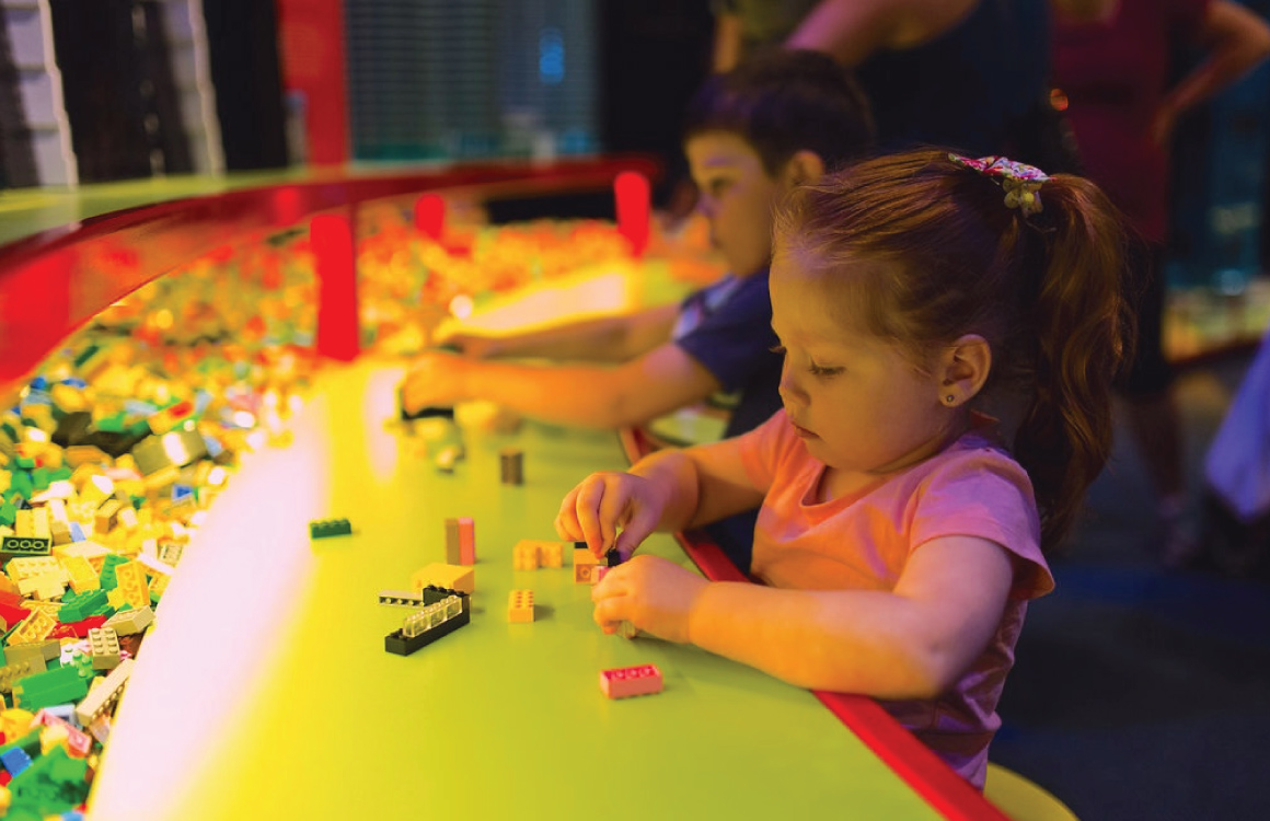 Kids build with Lego bricks at a table.” width=