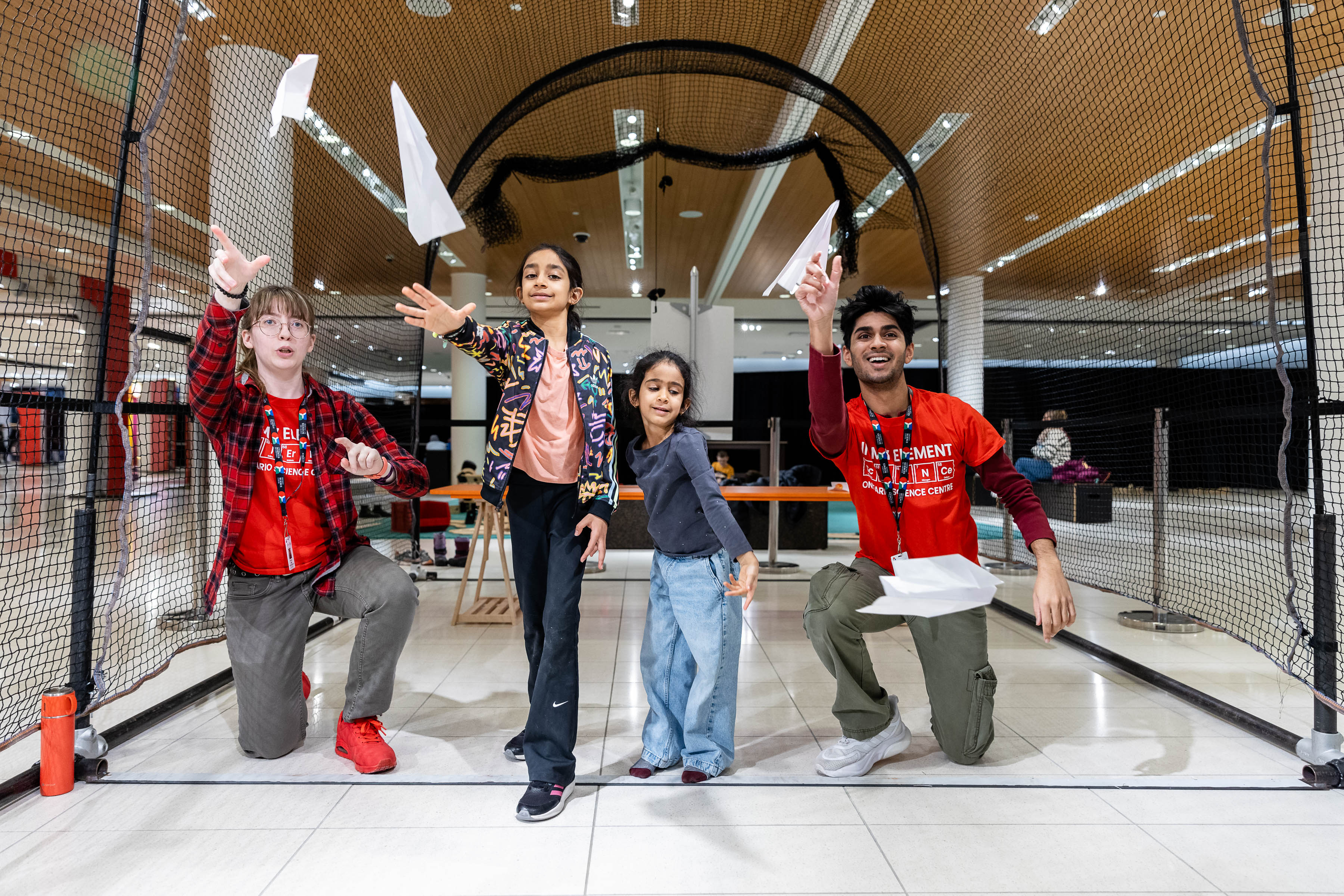 Two kids throwing the paper airplanes along with two staff members at CF Sherway Gardens.