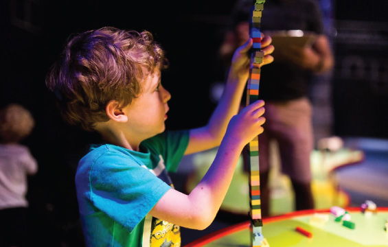 A kid build a tall tower with Lego bricks.