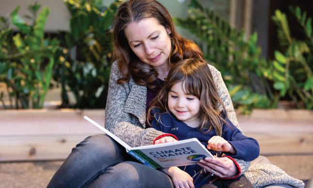 A woman reads a book called "Climate Change" with a child.