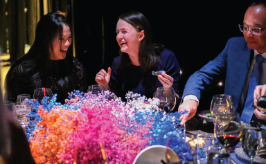 Three guests eat and laugh at a dinner table.